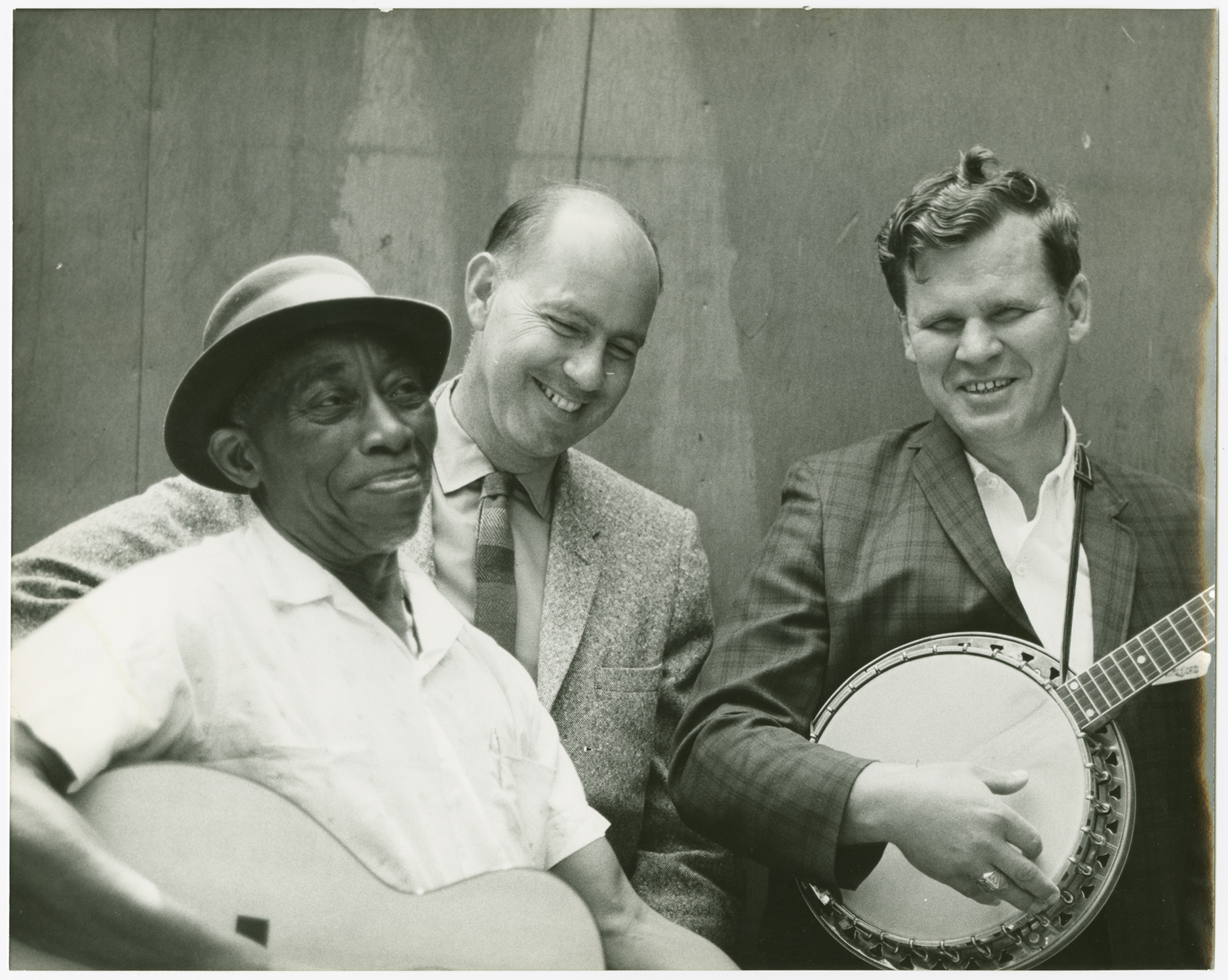 A photograph showing "Mississippi" John Hurt holding a guitar, Sam Hinton, and Arthel "Doc" Watson holding a banjo at the Berkeley Folk Music Festival, 1964